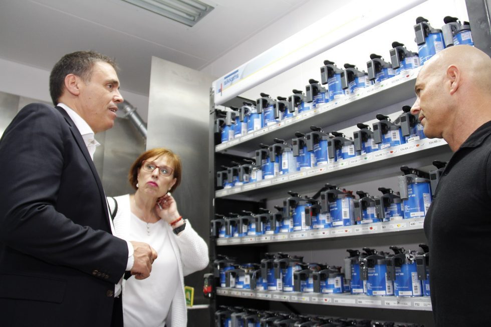 tres personas conversando frente a una estantería llena de botes de pintura.