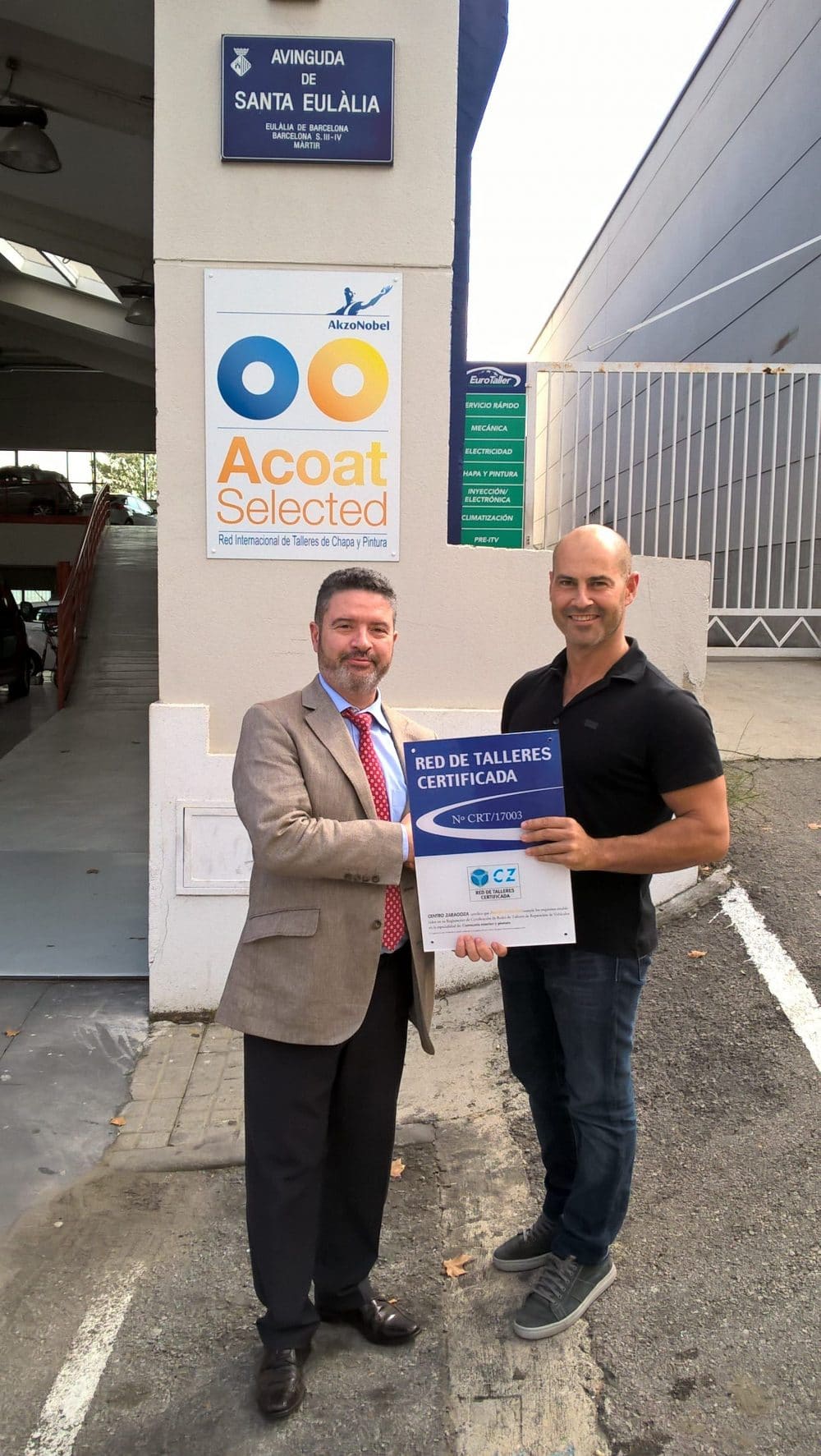 Dos representantes posan frente a las instalaciones del taller, sosteniendo orgullosamente la placa de certificación de la Red Acoat Selected otorgada por el Instituto Centro Zaragoza